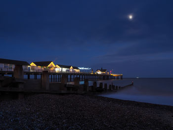 Illuminated buildings by sea against sky at night