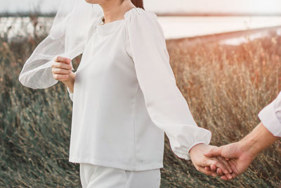 Cropped image of man holding woman hand while standing on field