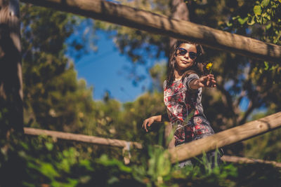 Teenage girl wearing sunglasses standing against trees in forest