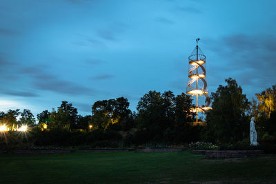 Trees by illuminated building against sky at dusk