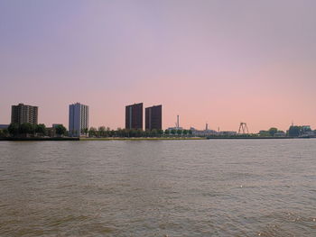 Sea by buildings against clear sky during sunset