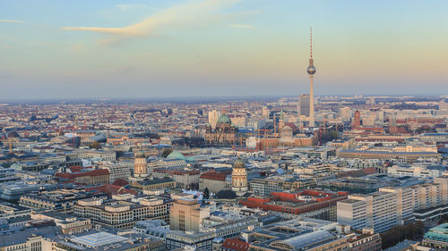 Fernsehturm amidst cityscape against sky during sunset