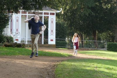 Full length of boy running while sister walking in background at park