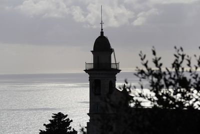 Lighthouse on building by sea against sky