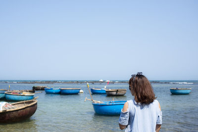 Rear view of woman standing against basket boats at beach