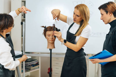 Professional hairdresser teaching adult students how to use hairdressing scissors during course 