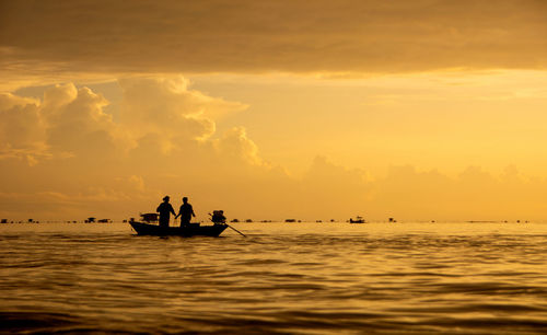Silhouette fishermen on wooden boat preparing casting a net catching fish in the early morning