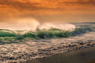 Waves splashing on shore against sky during sunset