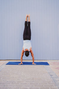 Full length of man doing yoga on exercise mat against wall