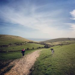 Scenic view of girl and dog on landscape against cloudy sky