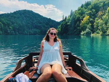 Young woman sitting on boat in lake against trees