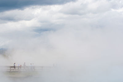 People on bridge against sky during foggy weather