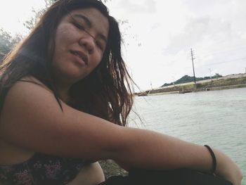 Portrait of smiling young woman sitting against sky