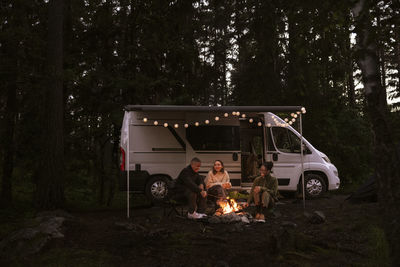 Friends camping in forest and sitting by campfire