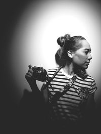 Woman holding camera while looking away against wall