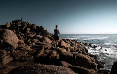 Man standing on rock by sea against clear sky