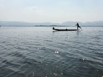 Silhouette fisherman on boat over lake against sky