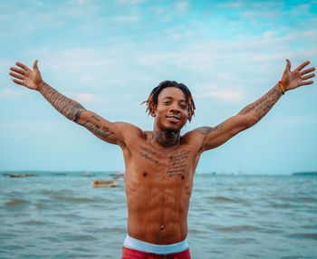 Portrait of shirtless man standing at sea against sky