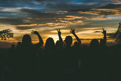 Silhouette people making love text with hands against sky during sunset