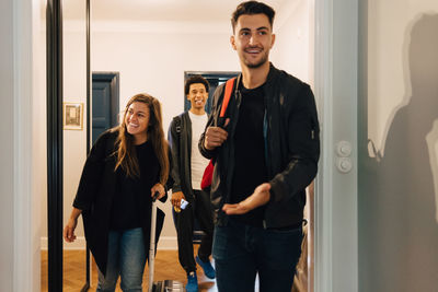 Smiling young friends arriving with luggage at rental apartment