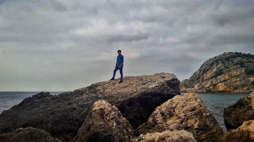 Rear view of man standing on cliff by sea against sky