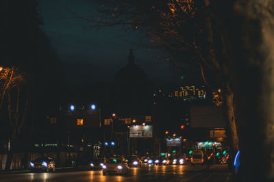 Illuminated street by buildings in city at night
