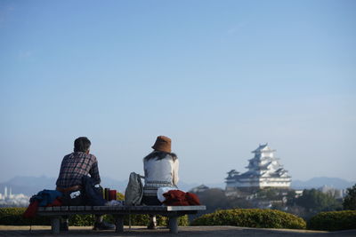 People sitting on bench with building in background