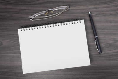 Directly above view of office wooden table with pen, notepad and reading glasses. flat lay.