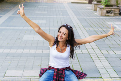 Happy young fashion woman sitting on the street sidewalk stylish female model