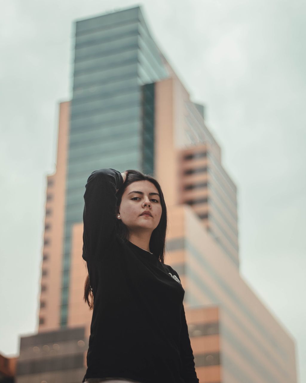 architecture, built structure, building exterior, one person, standing, women, low angle view, city, lifestyles, real people, focus on foreground, adult, young adult, leisure activity, young women, sky, building, day, front view, outdoors, office building exterior, hairstyle, skyscraper, teenager, contemplation