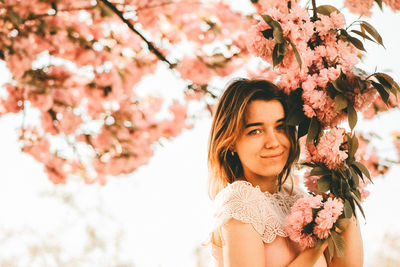 Portrait of beautiful woman standing by cherry blossom tree