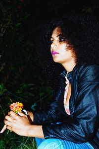Young woman looking down while sitting by flower