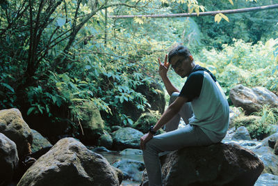 Side view portrait of man sitting on rock in forest