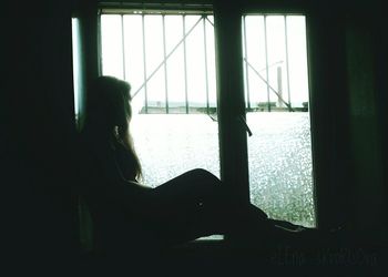 Silhouette woman looking through window at home