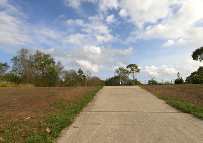 Empty road amidst trees on field against sky