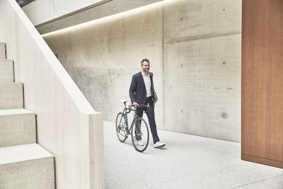 Businesssman pushing bicycle along concrete wall