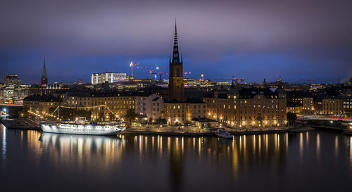 Illuminated buildings by river in city at night