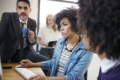 Businesswoman working on computer by colleagues at desk in office