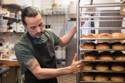 Confident mature male owner holding metallic rack at bakery kitchen