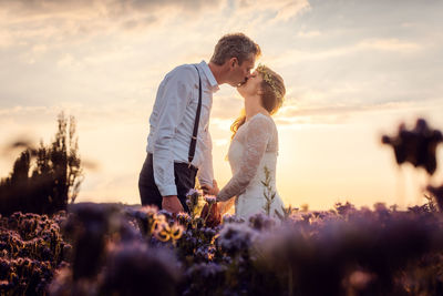 Couple kissing in farm against sky during sunset
