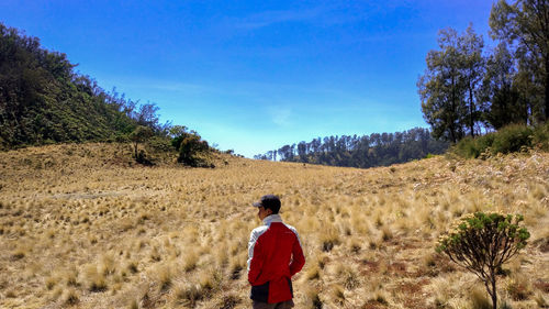 Rear view of man looking away while standing on field against sky