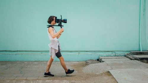 Side view of young man photographing while walking on street