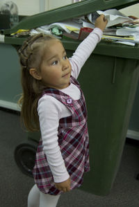 Side view of cute girl holding paper in garbage can