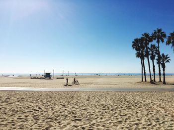 Mid distance view of person cycling at beach against clear blue sky