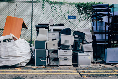 Abandoned stacked computer printers against fence