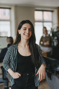 Portrait of young entrepreneur with hand in pocket leaning on chair at office