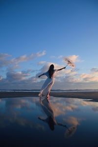 Young woman jumping on beach against sky during sunset