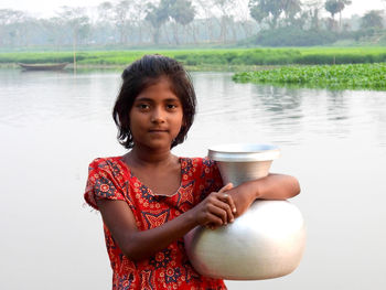 Portrait of smiling young woman holding water at lakeshore