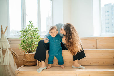 Mother with baby son on a wooden bench against the background of the window