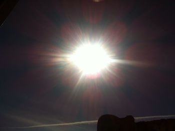 Low angle view of sun shining through clouds